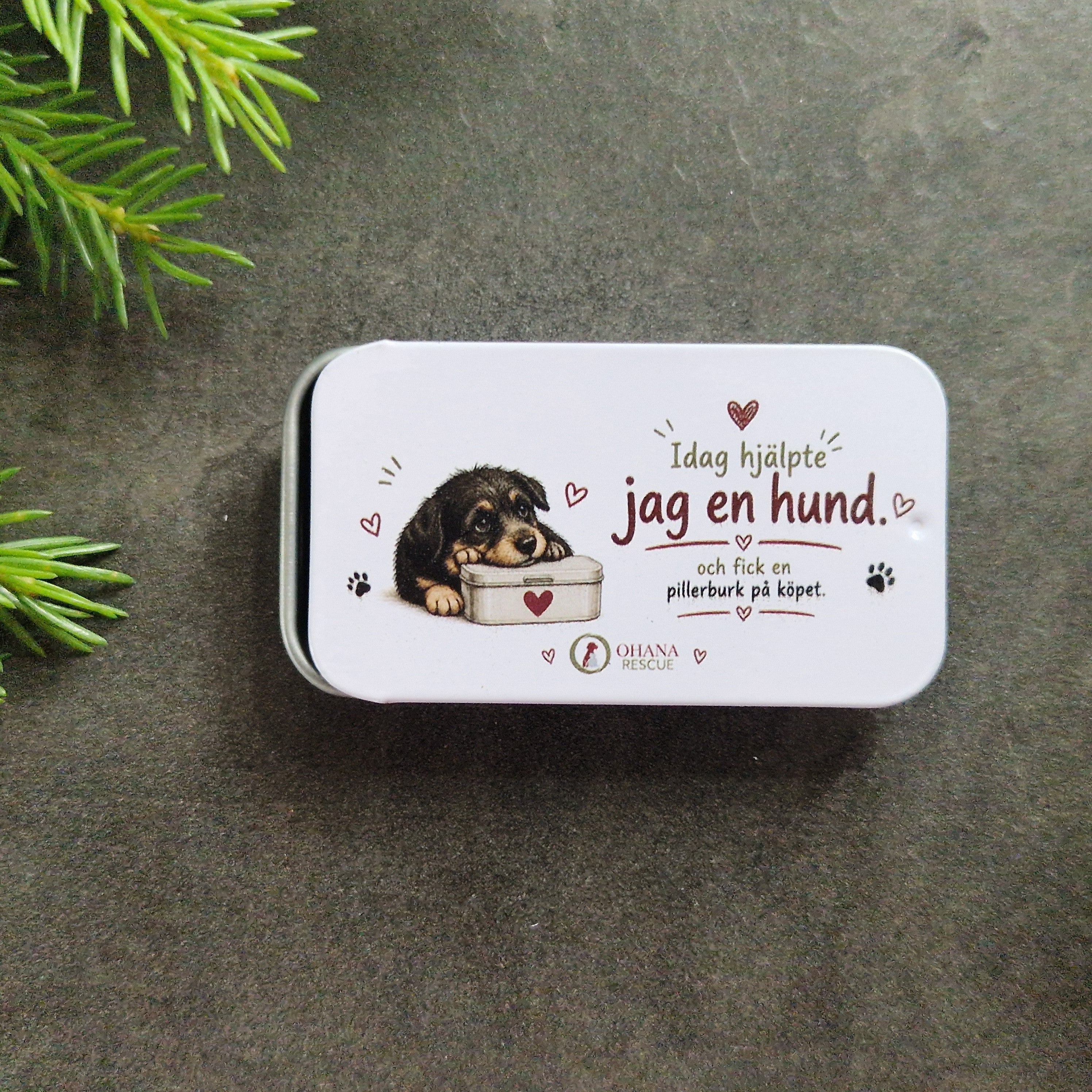Närbild på liten plåtask med texten Idag hjälpte jag en hund och fick en pillerburk på köpet